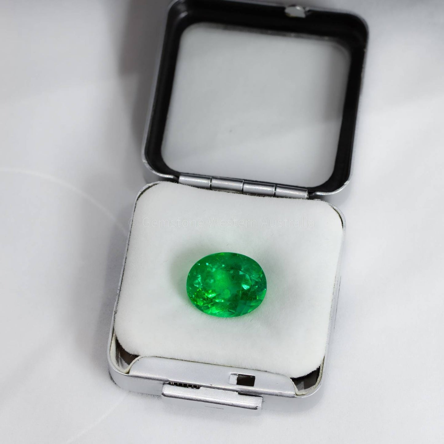 Oval green gemstone displayed in white jewelry box with soft cushion