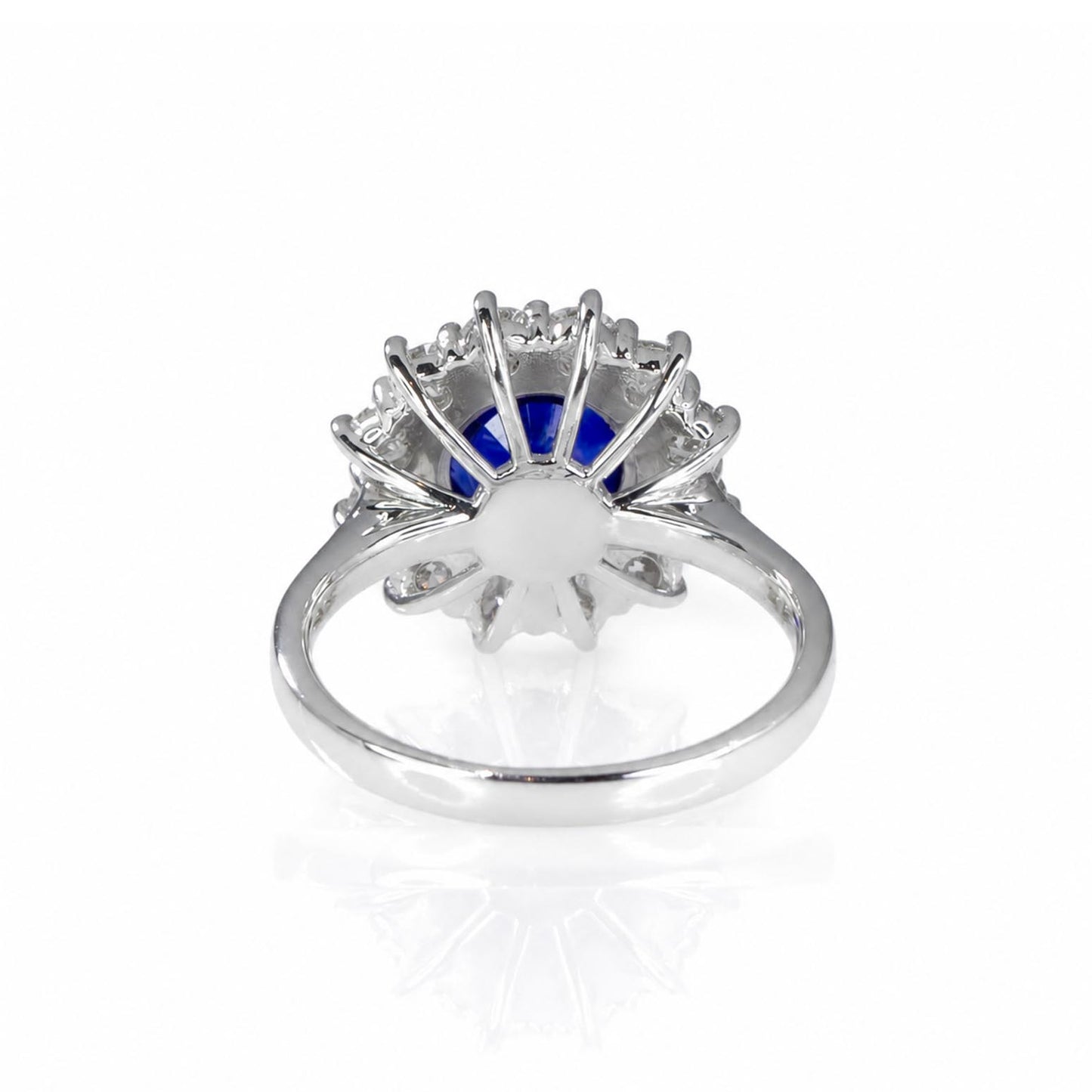A platinum ring featuring a central round blue sapphire surrounded by a halo of round brilliant-cut diamonds, shown from the back on a white background with a soft reflection.