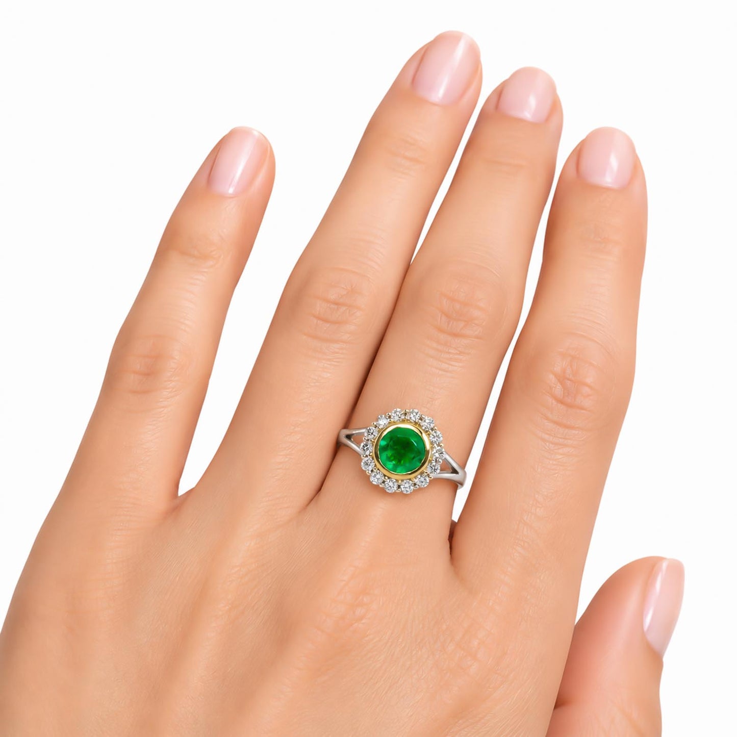 A white and yellow gold ring with a round Colombian emerald surrounded by a halo of diamonds, shown worn on a hand against a white background.