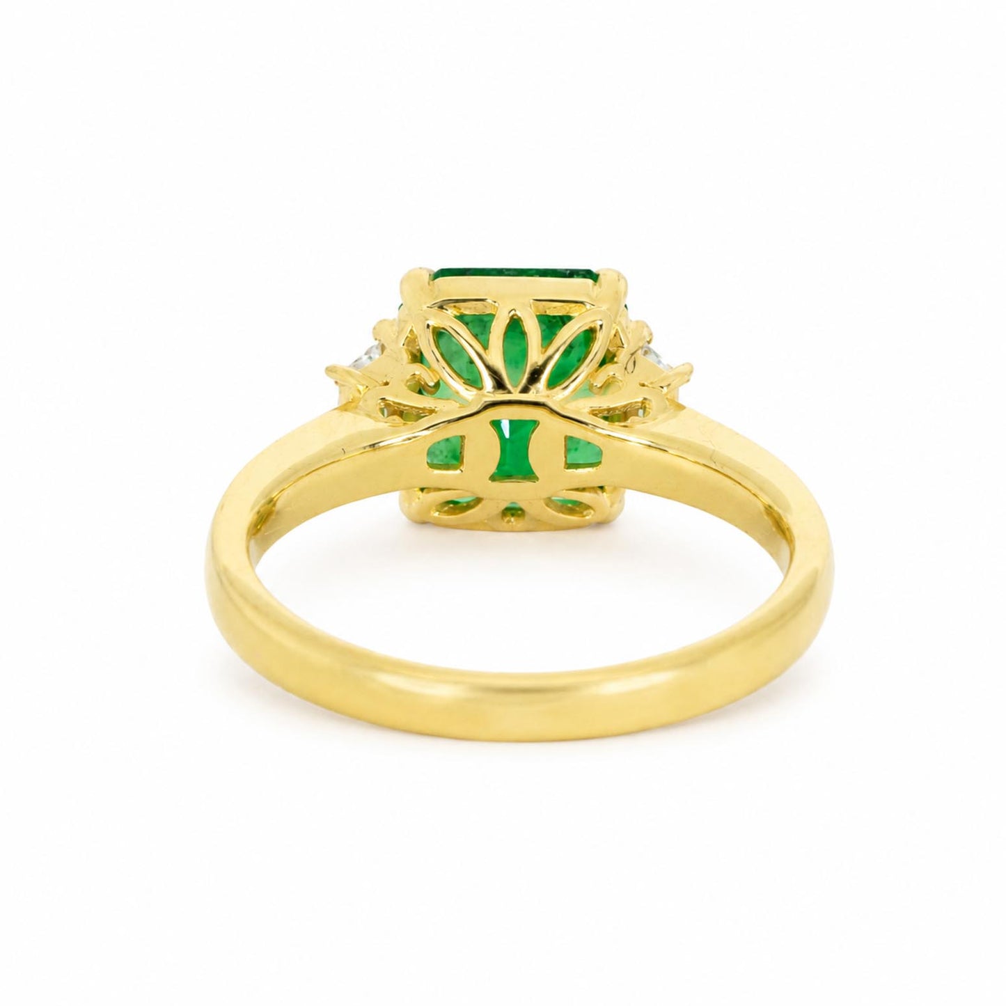 back view of a yellow gold ring featuring an emerald-cut Colombian emerald center stone and a floral setting shown on a plain white background.