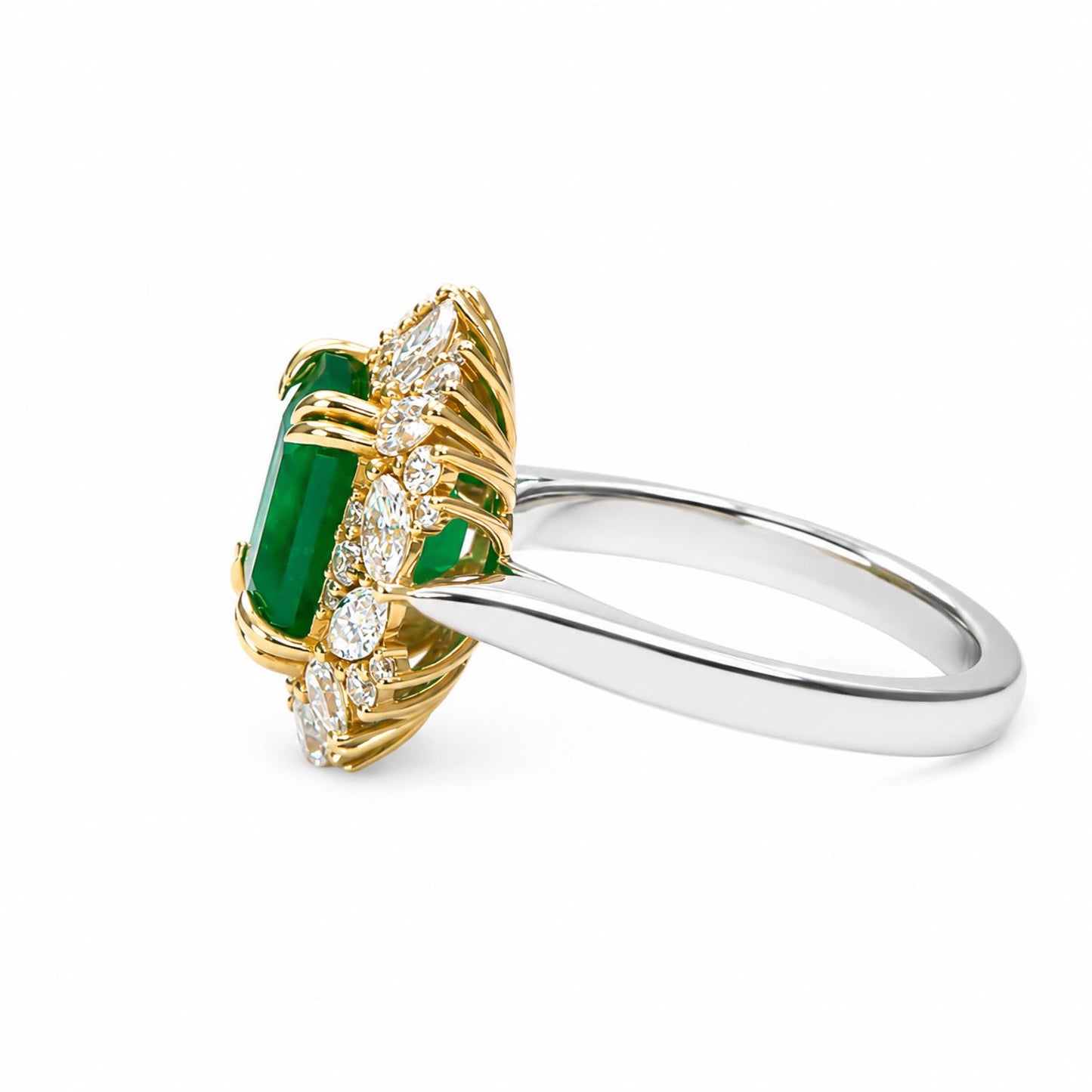 A yellow gold ring featuring a large emerald-cut emerald gemstone, surrounded by smaller round, pear and marquise-cut diamonds, set on a polished platinum band, shown against a plain white background.