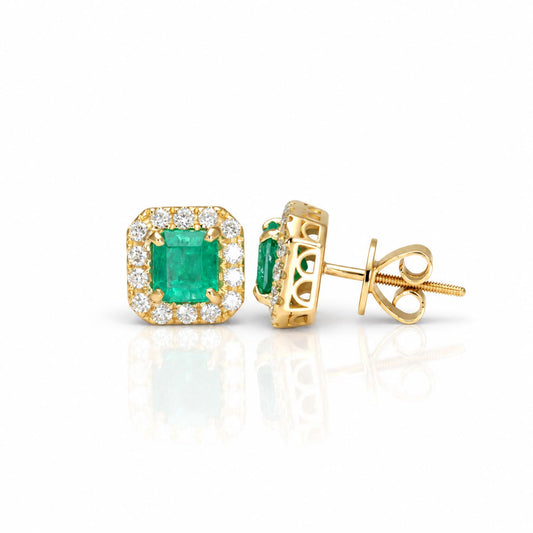 A pair of yellow gold stud earrings featuring emerald-cut Colombian emerald gemstones surrounded by a halo of small diamonds, shown on a white background with one earring facing forward and the other angled to show the post and butterfly back.