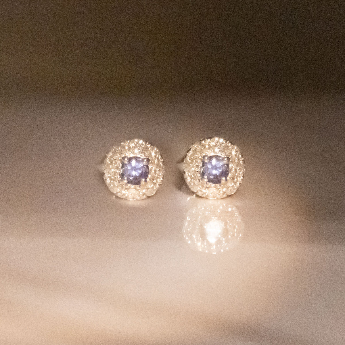 a pair of alexandrite stud earrings photographed under incandescent light showing the colour change of alexandrites.