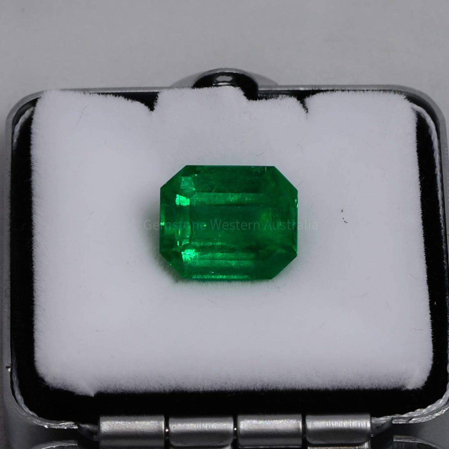 Emerald cut vivid green emerald gemstone in display box on white cushion