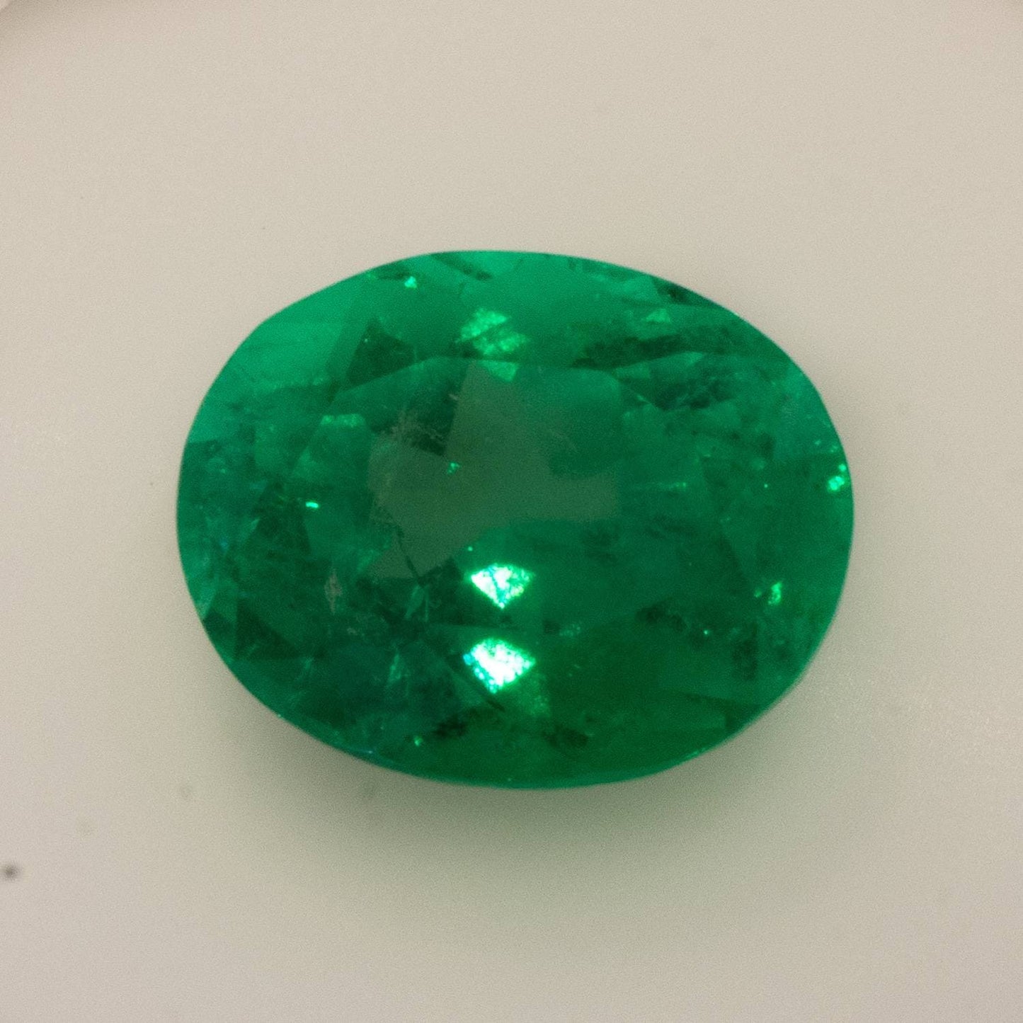 Oval-cut green emerald gemstone with visible inclusions on white soft.