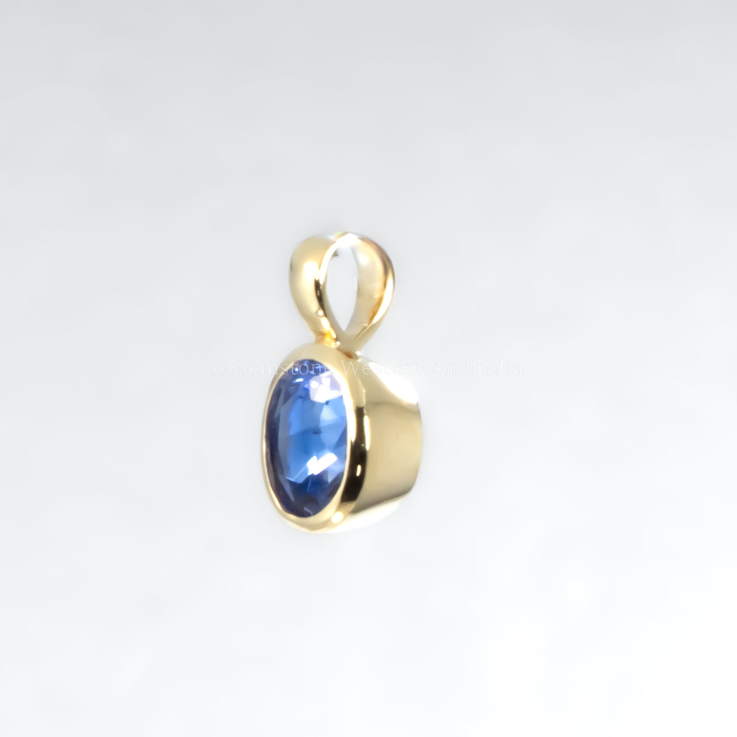 Gold pendant with a blue gemstone on a light gray background