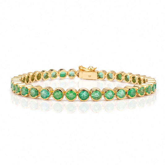 A yellow gold tennis bracelet with Colombian emeralds on a white background