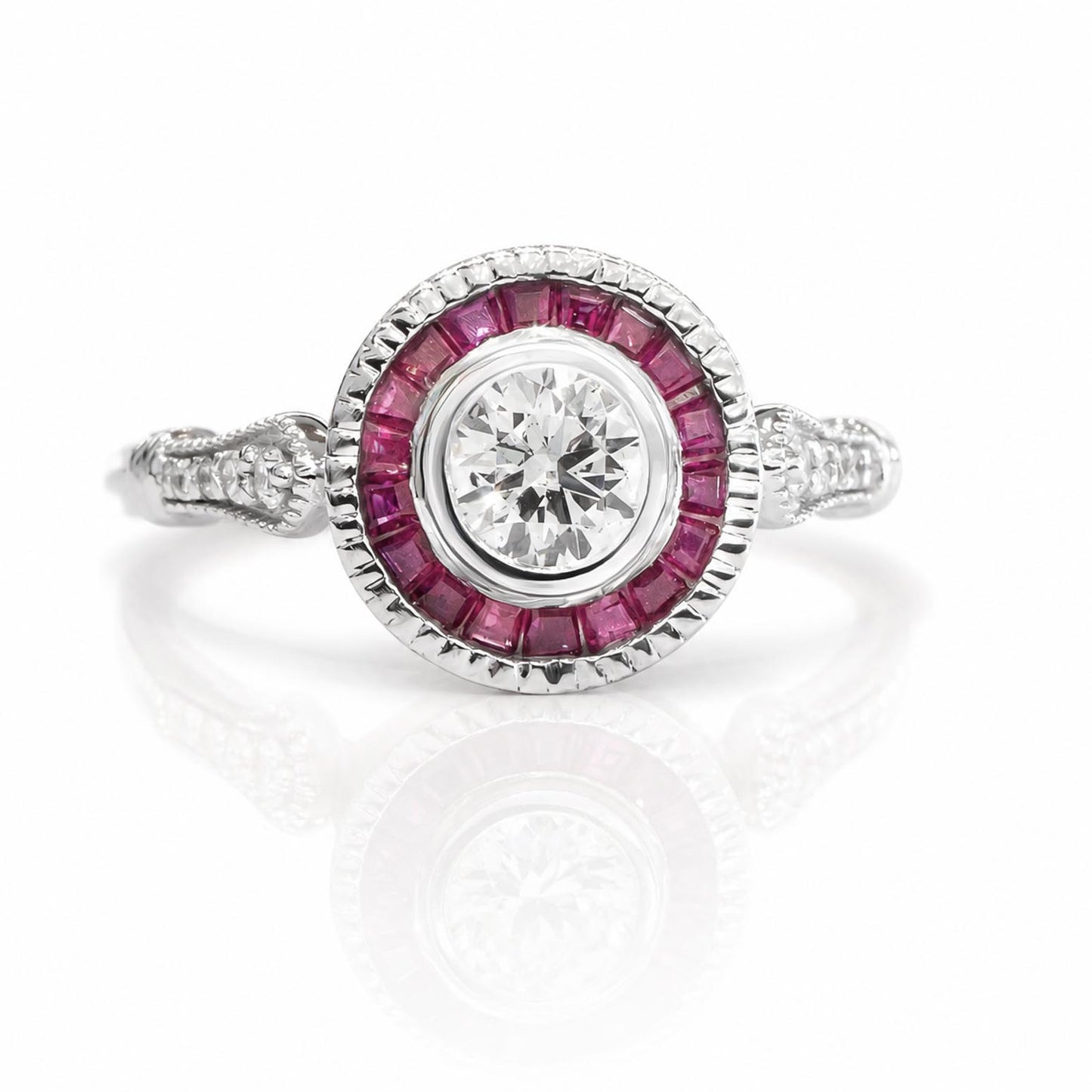 A white gold diamond ring featuring a round-cut center diamond surrounded by a halo of custom cut baguette rubies, with accent sise diamonds on the band, shown on a white background with a soft reflection.