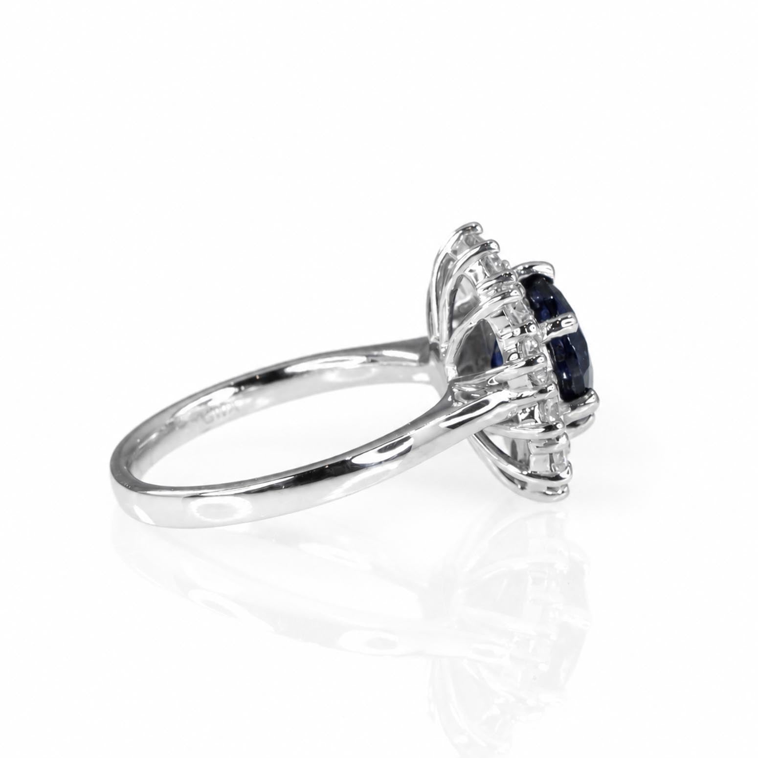 Side view of a platinum ring featuring a central round blue sapphire gemstone surrounded by round brilliant-cut diamonds, shown on a clean white background with a soft reflection below.