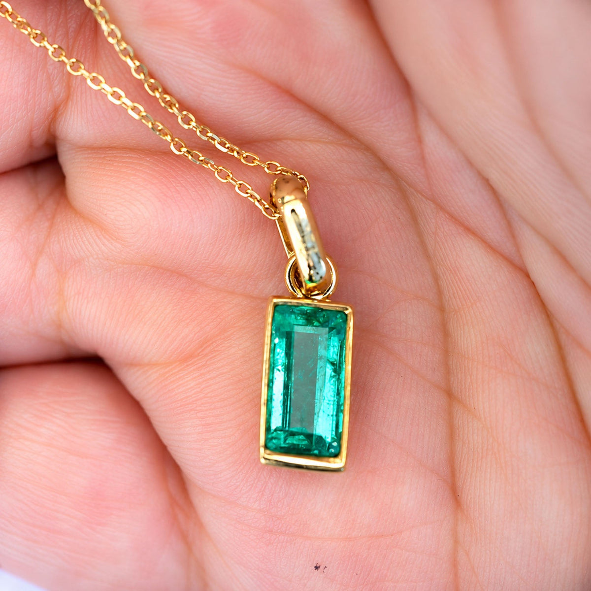 Colombian emerald pendant in the palm of the hand, gold bezel setting