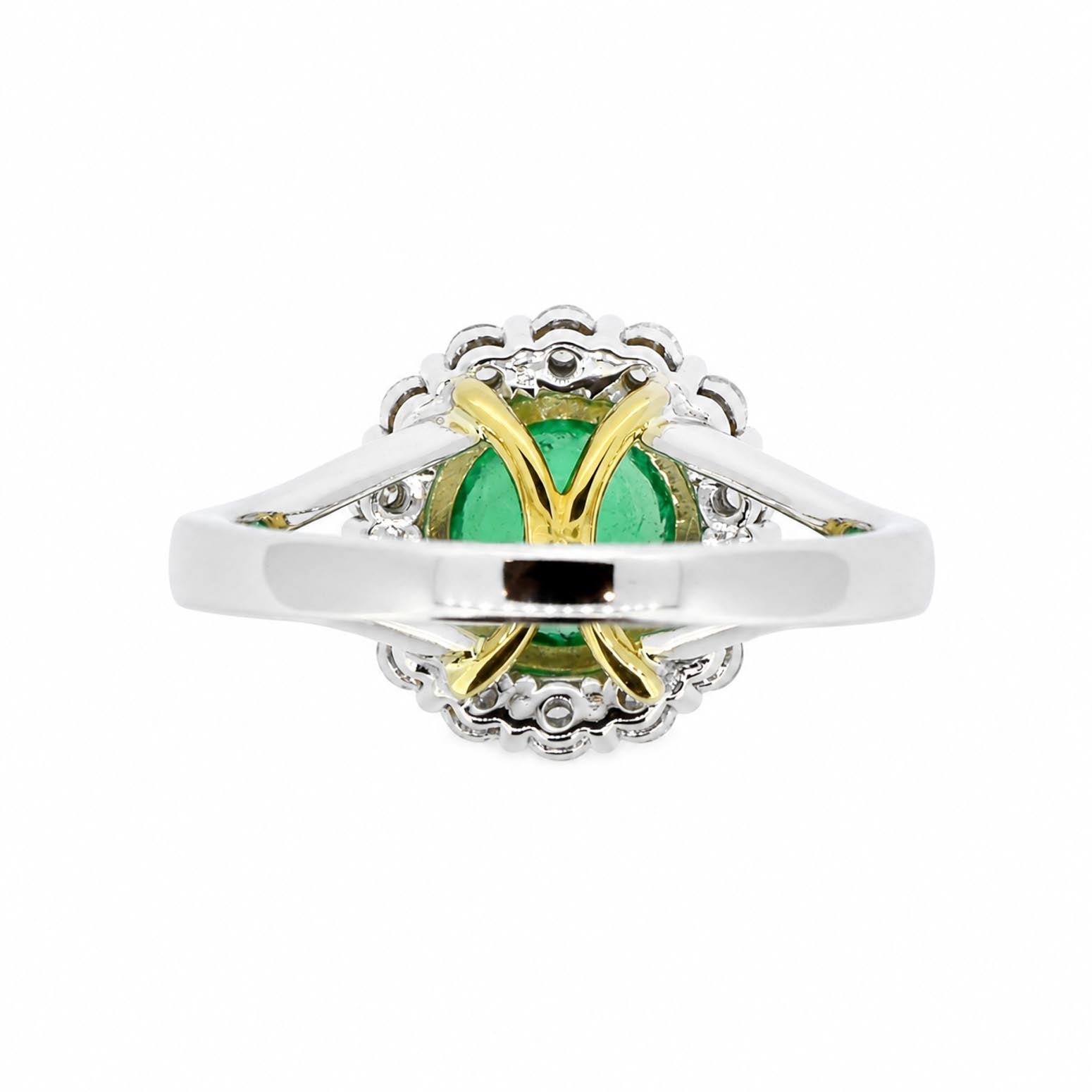 back view of a white and yellow gold ring featuring a central emerald, surrounded by diamonds in a floral halo setting.