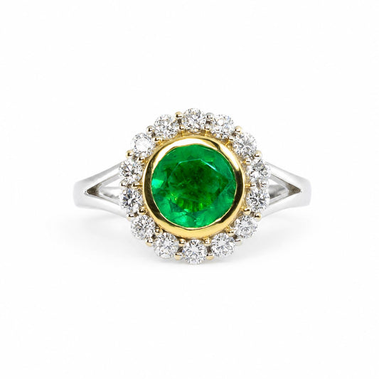 A round-cut natural Colombian emerald ring with a halo of diamonds and a gold inner bezel, set on a white gold split shank band.
