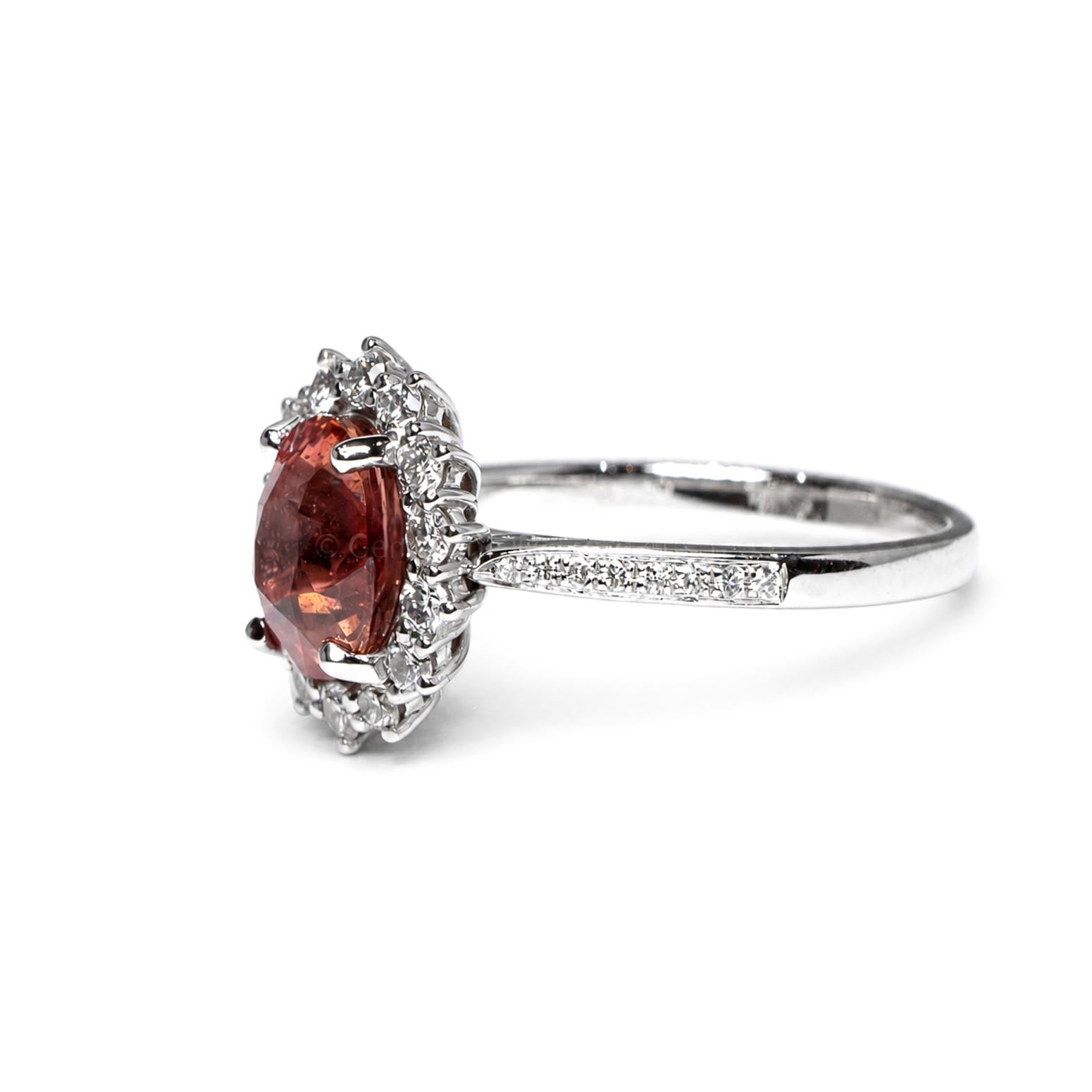 Side view of a platinum ring featuring a large oval padparadscha sapphire center stone surrounded by diamonds. Accent diamonds in a pavé setting on a platinum band, shown on a white background.