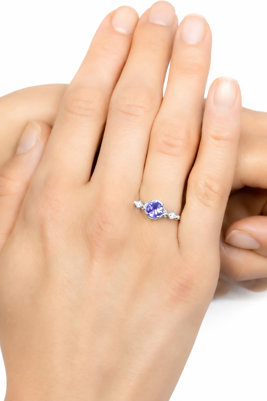 A white gold ring with a round purple sapphire and small side diamonds, shown worn on a person's ring finger against a white background.