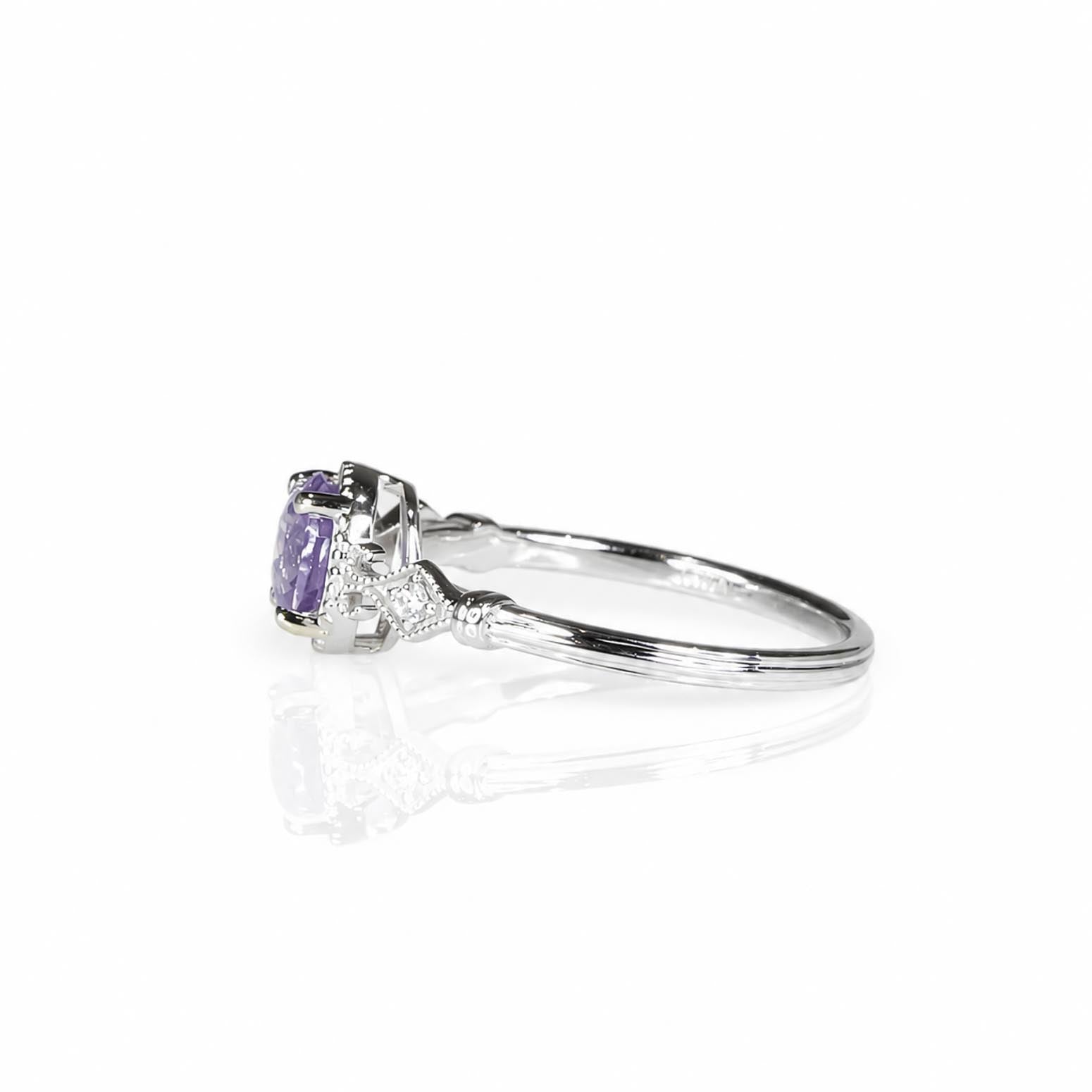 Side view of a white gold ring with a round violet sapphire and diamond accented shoulders in a white background