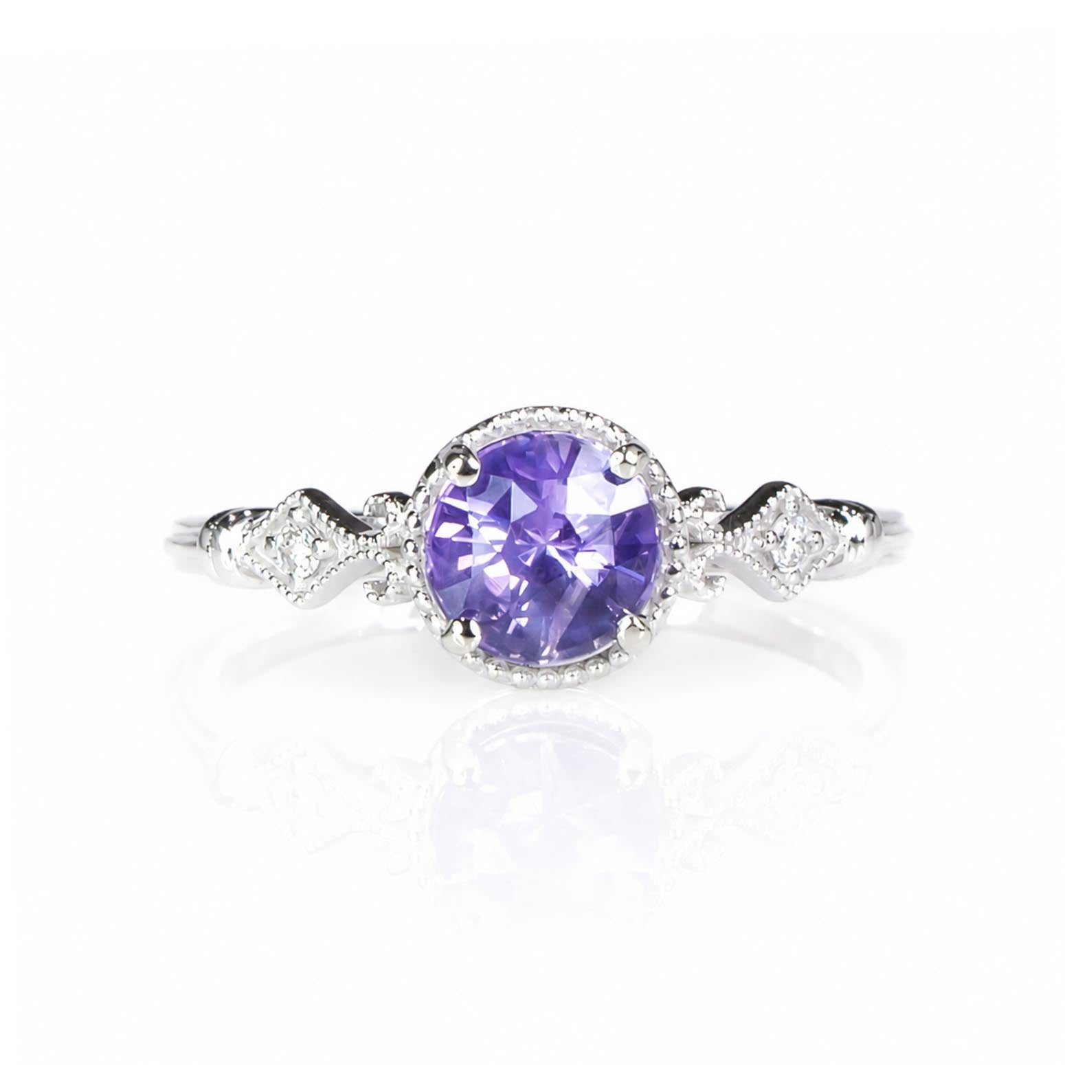 A white gold diamond ring featuring a round purple sapphire center stone in a halo setting, with diamond-accented shank on a white background.
