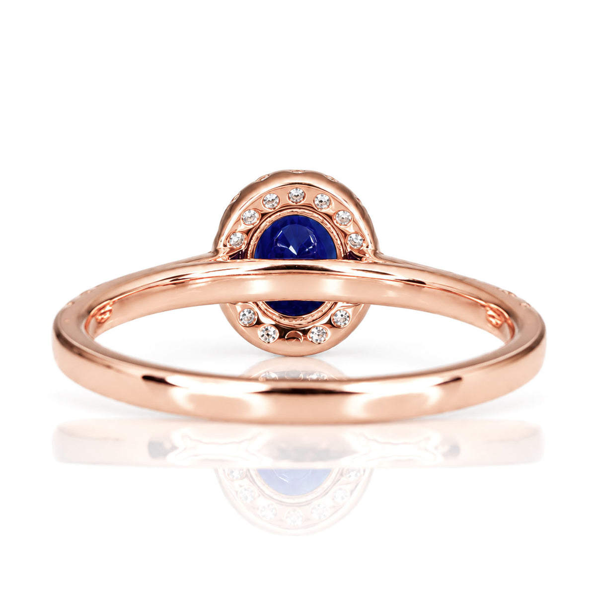 view of the back of a rose gold ring with an oval cut, natural blue sapphire surrounded by a halo of diamonds, shown on a white background 