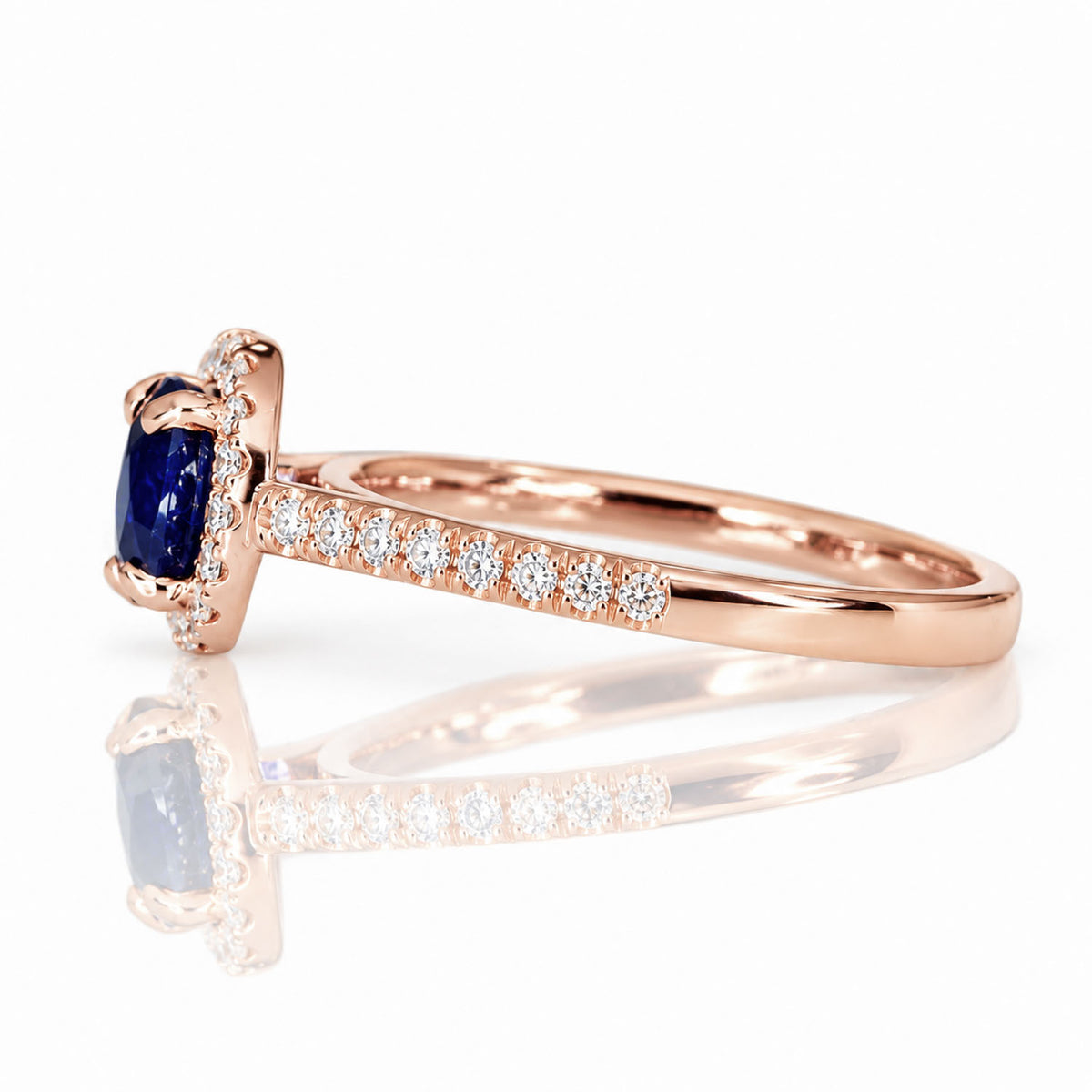 view of the side profile of rose gold ring with an oval cut blue sapphire surrounded by a halo of diamonds and diamonds on the shank