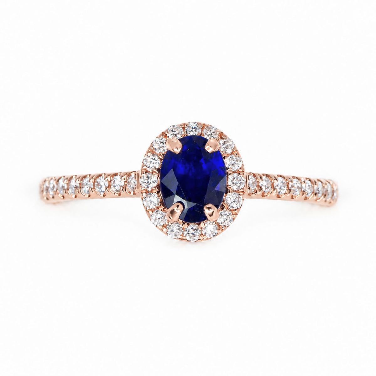 front view of a rose gold ring with an oval cut, natural blue sapphire surrounded by a halo of diamonds, shown on a white background 
