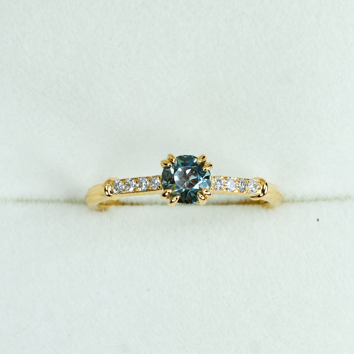Teal sapphire ring photographed on pale fabric
