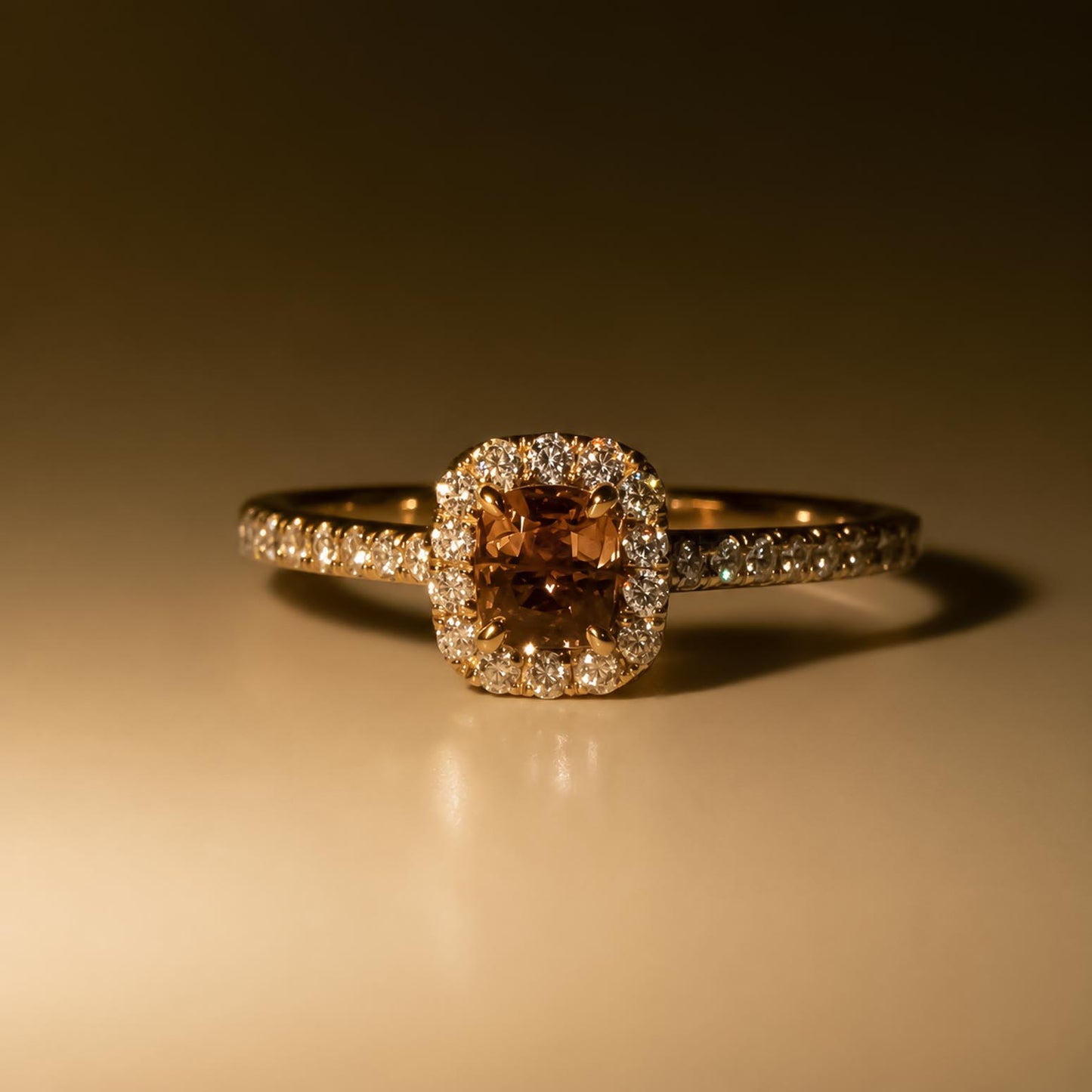 A rose gold halo ring featuring a cushion-cut alexandrite with a halo of diamonds and diamond side stones, photographed on a warm incandescent lighting and reflective surface.