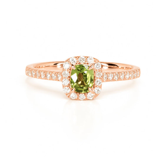 A rose gold ring with a natural alexandrite as centre gemstone surrounded by a halo of diamonds and diamond accents on the band in a white background 