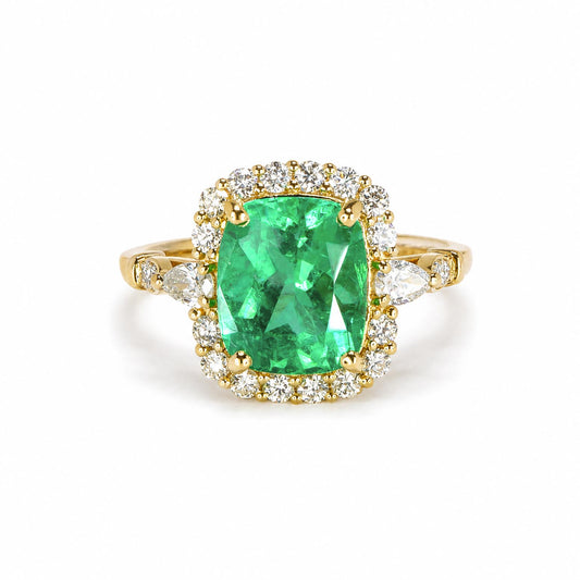 A yellow gold ring featuring a large cushion-cut natural Colombian emerald surrounded by a halo of round brilliant cut diamonds, with additional diamonds set along the shoulders of the band, shown on a plain white background.