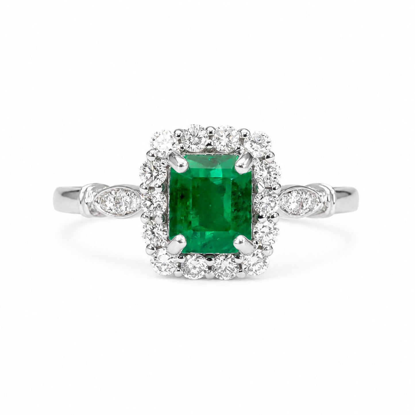 An emerald-cut Colombian emerald halo ring in a platinum setting, surrounded by a halo of diamonds, on a plain white background.
