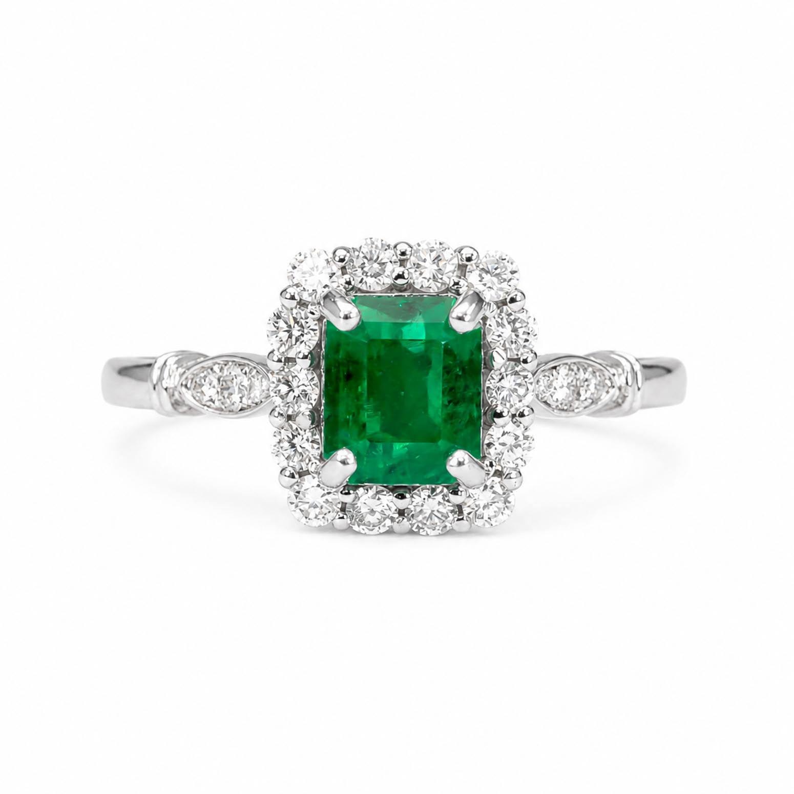 An emerald-cut Colombian emerald halo ring in a platinum setting, surrounded by a halo of diamonds, on a plain white background.