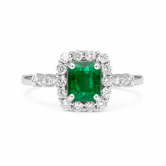 An emerald-cut Colombian emerald halo ring in a platinum setting, surrounded by a halo of diamonds, on a plain white background.