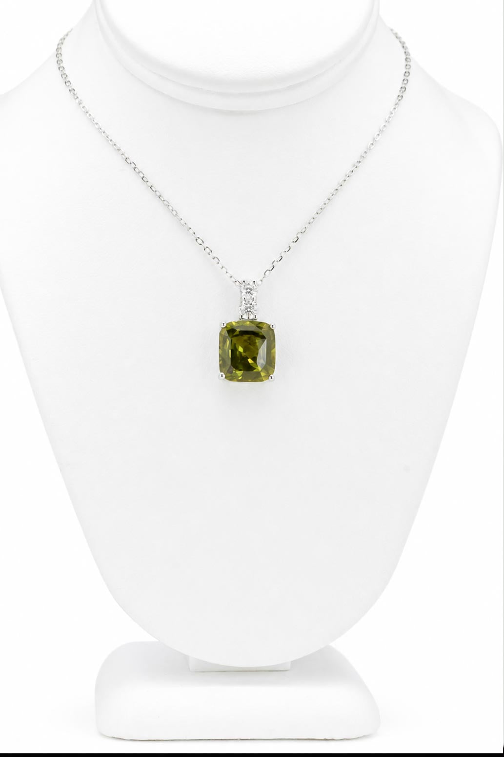 A platinum pendant holding a cushion cut green sapphire accented by two round brilliant cut diamonds on the bail shown on a jewellery display neck on a white background