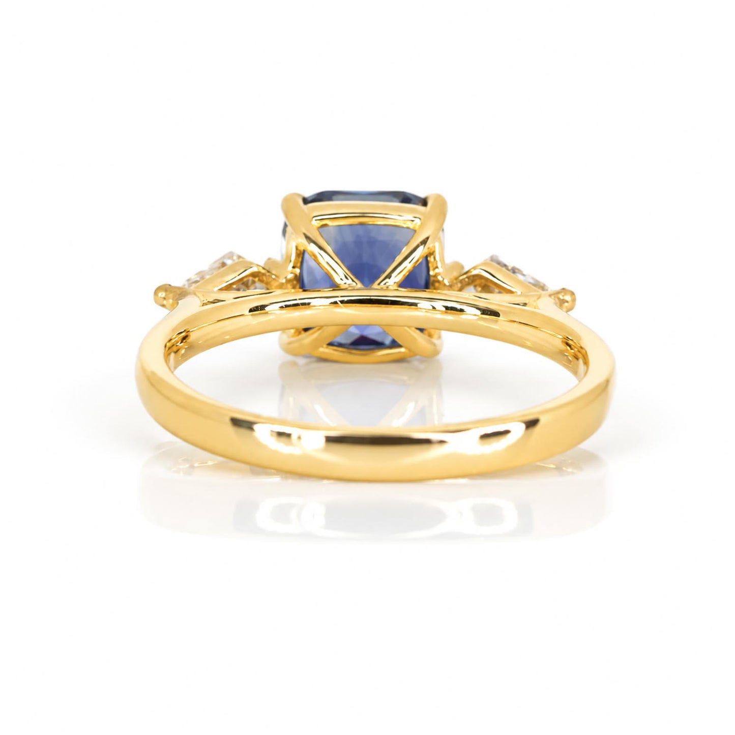 A view of the back of a polished yellow gold ring that holds a centre natural blue sapphire and side kite-cut diamonds 