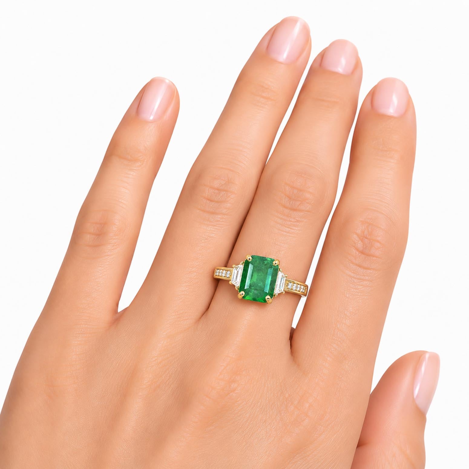 A gold ring with an emerald-cut Colombian emerald center stone and side diamonds, shown worn on a hand against a plain white background.