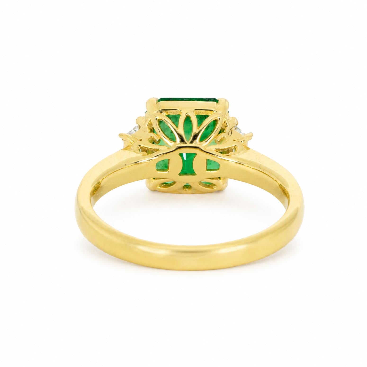 back view of a yellow gold ring featuring an emerald-cut Colombian emerald center stone and a floral setting shown on a plain white background.