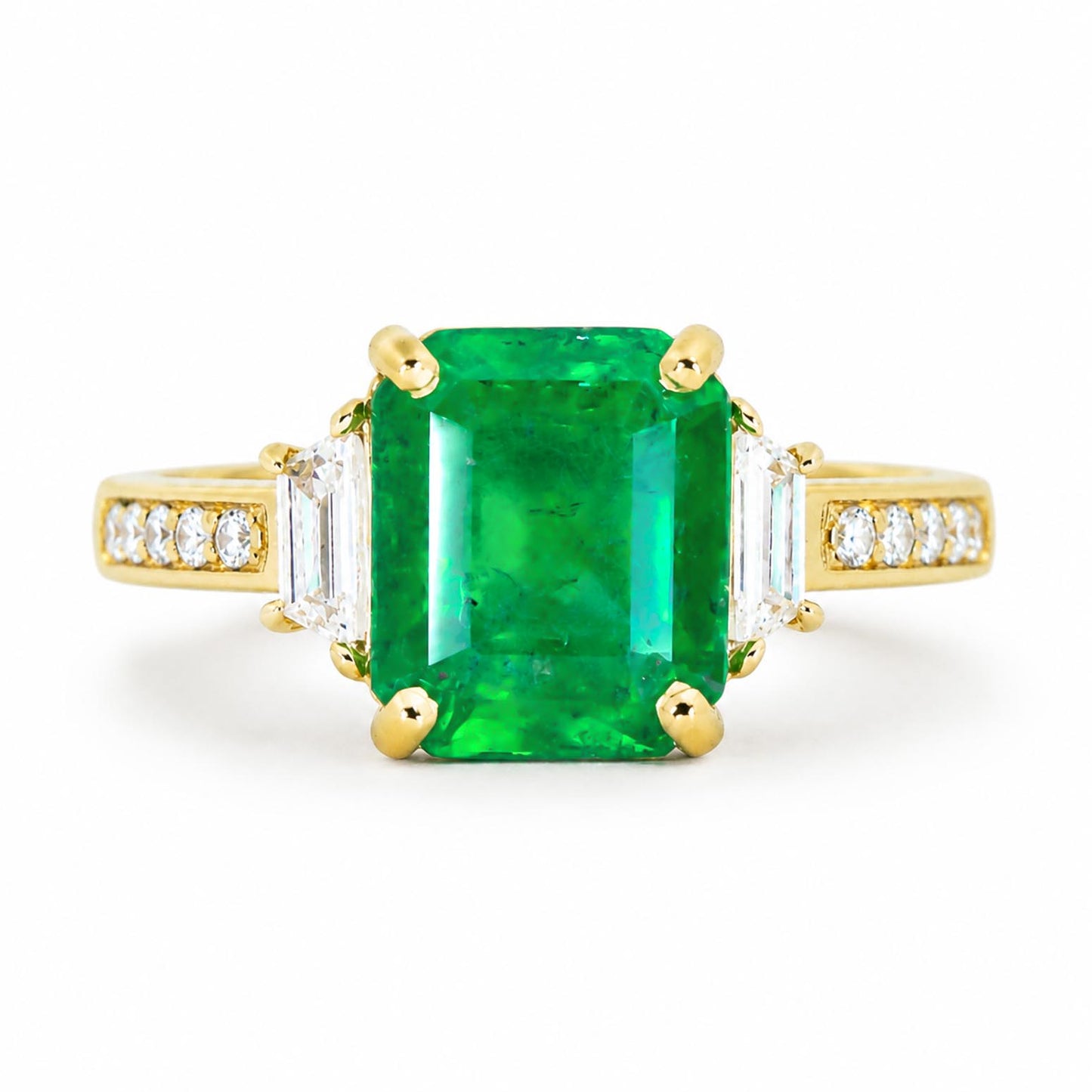 A yellow gold ring featuring a large emerald-cut Colombian emerald gemstone, flanked by baguette-cut side diamonds and a row of small round diamonds on the shoulders, set against a plain white background.