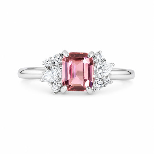 A platinum ring featuring a rectangular padparadscha sapphire in the center, flanked by two clusters of diamonds in different shapes, shown on a plain white background.