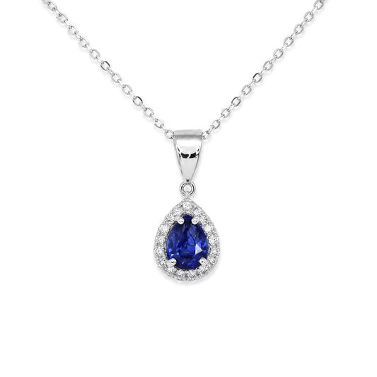 A blue sapphire pendant featuring pear-cut shape surrounded by round brillian-cut diamonds set in 18K white gold and shown on a white background 