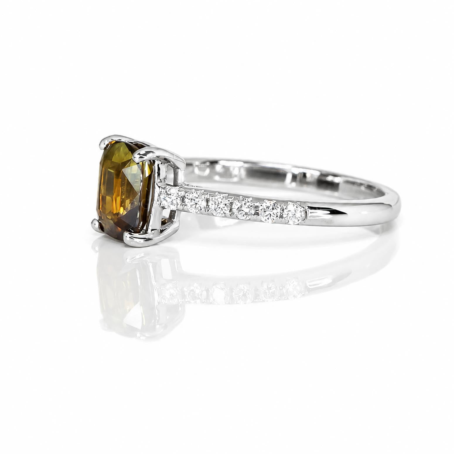 An 18K white gold ring featuring a cushion-cut alexandrite center stone and a pavé band set with diamonds, shown on a reflective white surface.