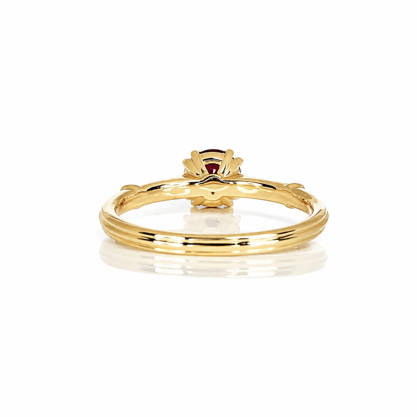 Back view of a yellow gold ruby ring with a double prong crown setting, shown on a clean white background with a soft reflection.