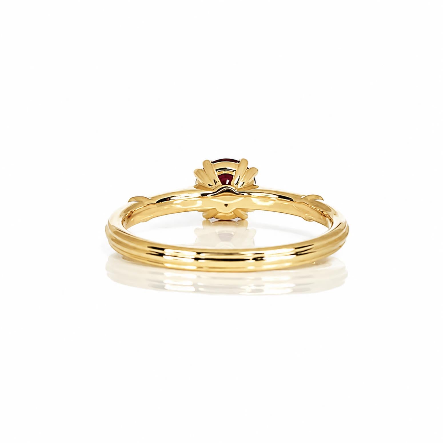 Back view of a yellow gold ruby ring with a double prong crown setting, shown on a clean white background with a soft reflection.
