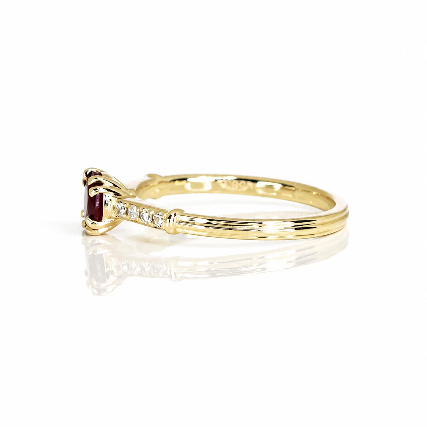 A yellow gold ring with a round natural ruby and a row of small diamonds on the band, shown on a white background with a soft reflection.