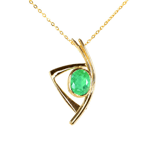 A yellow gold pendant featuring an oval cut Colombian emerald bezel set in a freeform gold pendant in a white background