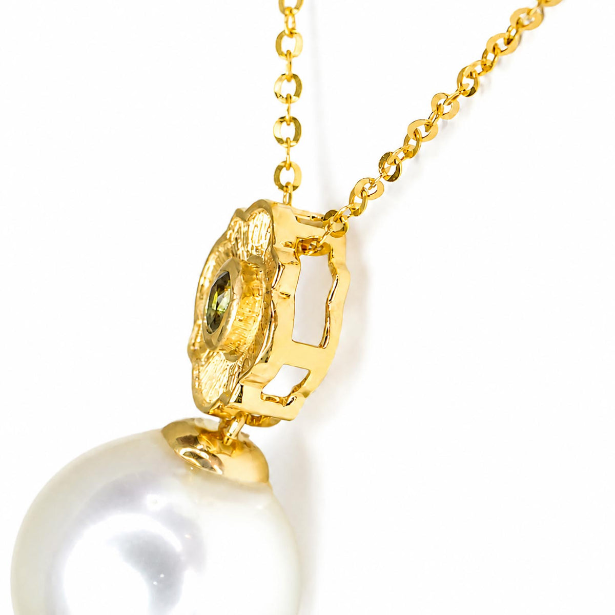 A close-up of a gold pendant necklace featuring a textured gold cap with a small oval-cut natural alexandrite and a large white pearl hanging below, on a white background.