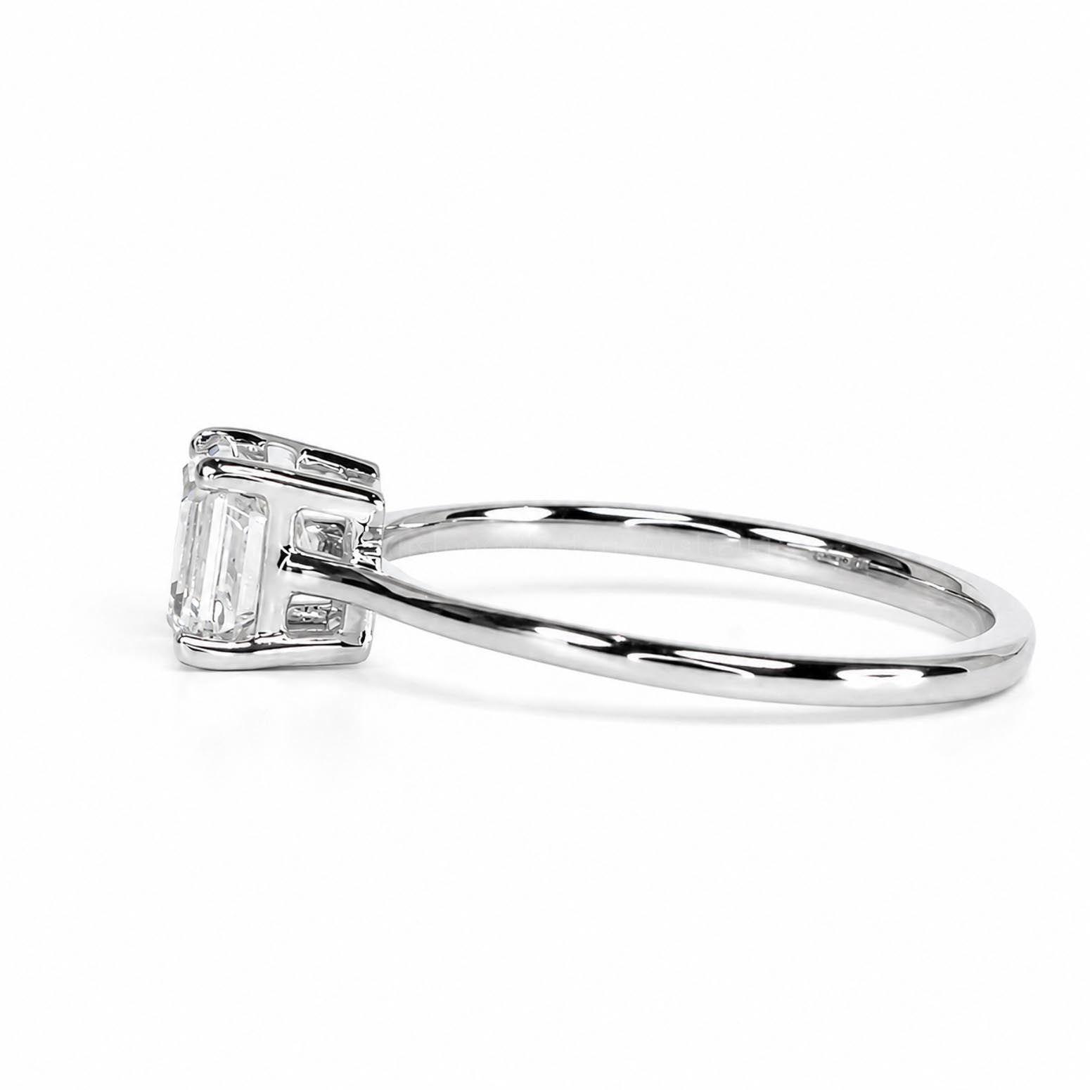 Side view of an emerald cut diamond engagement ring on a polished platinum band on a white background