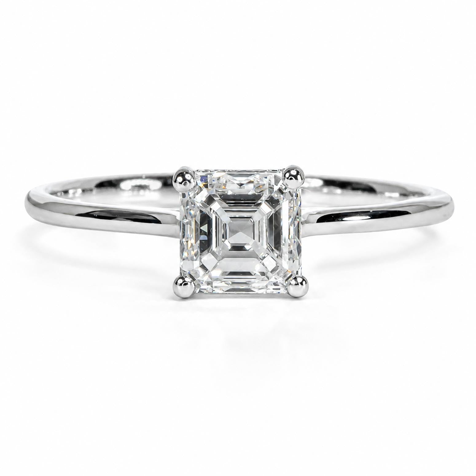 An emerald-cut diamond engagement ring in a polished platinum band, centered on a clean white background.