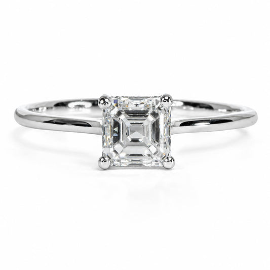 An emerald-cut diamond engagement ring in a polished platinum band, centered on a clean white background.