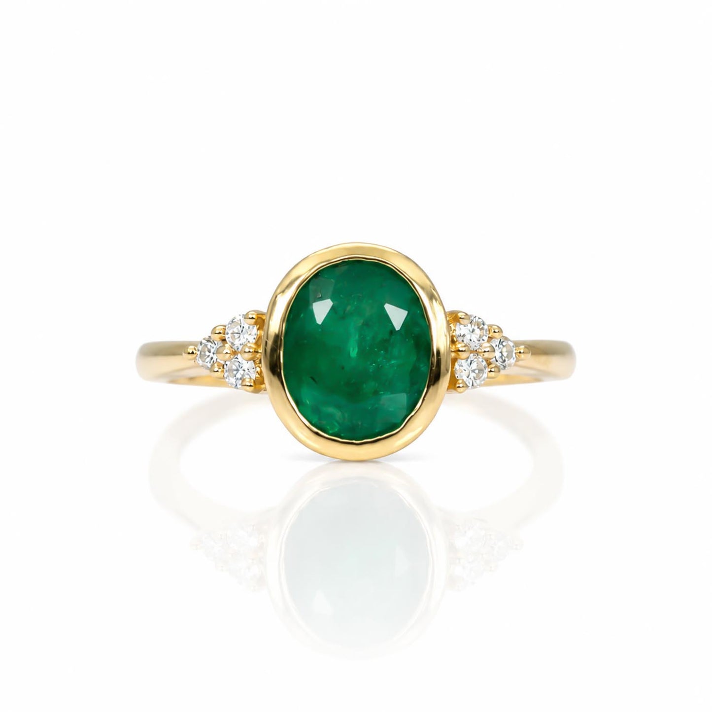 A yellow gold ring featuring an oval-cut natural Colombian emerald center stone, accented by small round diamonds on either side of the band, set against a clean white background with a soft reflection.