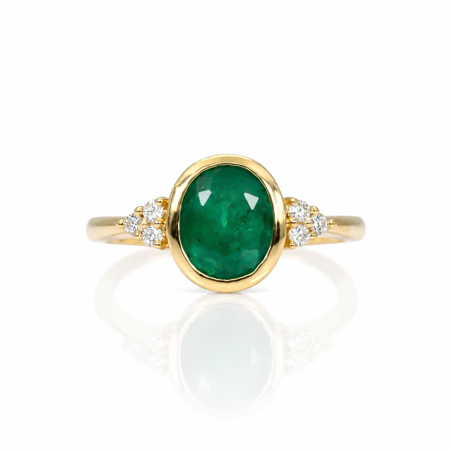 A yellow gold ring featuring an oval-cut natural Colombian emerald center stone, accented by small round diamonds on either side of the band, set against a clean white background with a soft reflection.