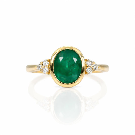 A yellow gold ring featuring an oval-cut natural Colombian emerald center stone, accented by small round diamonds on either side of the band, set against a clean white background with a soft reflection.