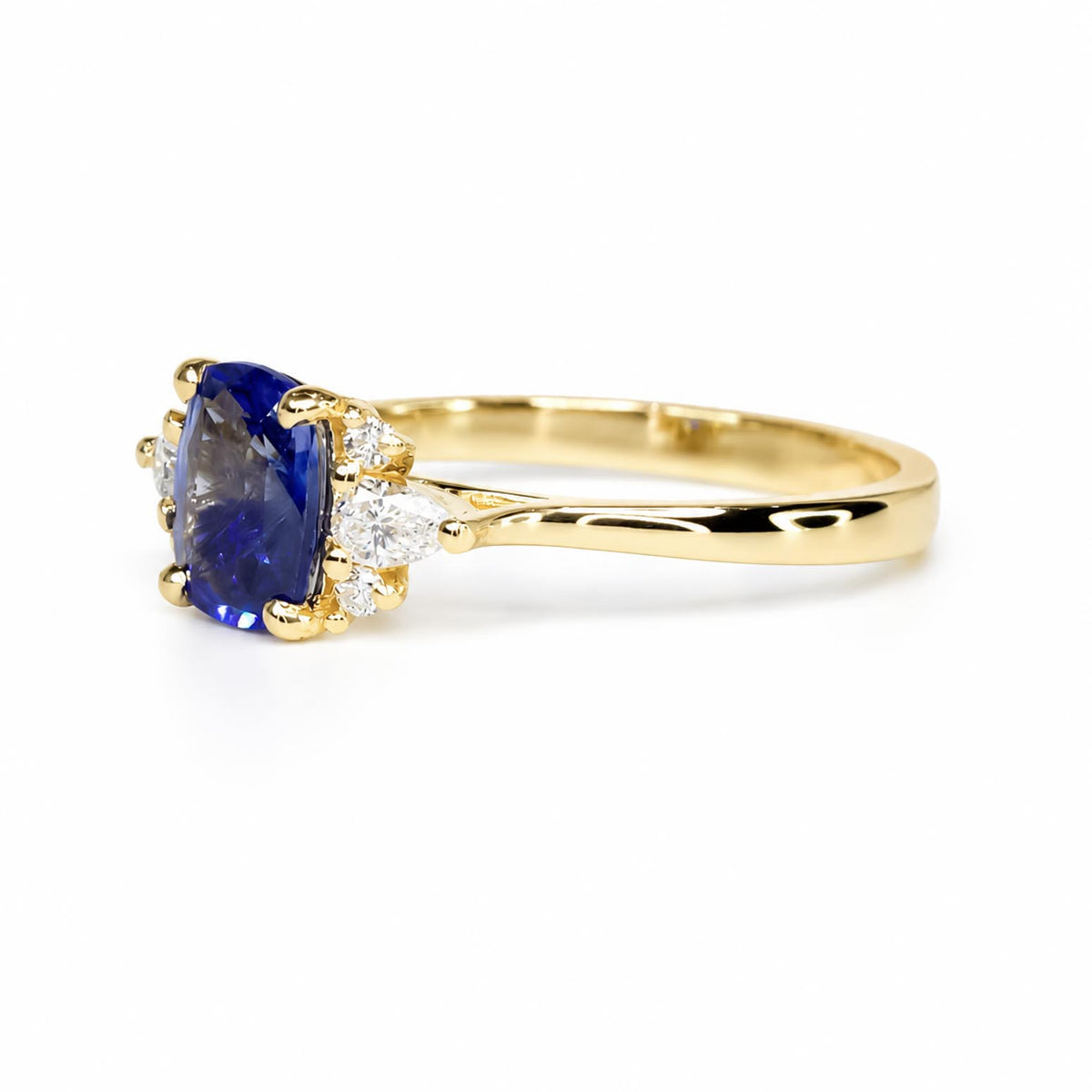 Side view of a yellow gold ring featuring a cushion-cut natural blue sapphire and side diamonds on a polished gold band shown on a white background 